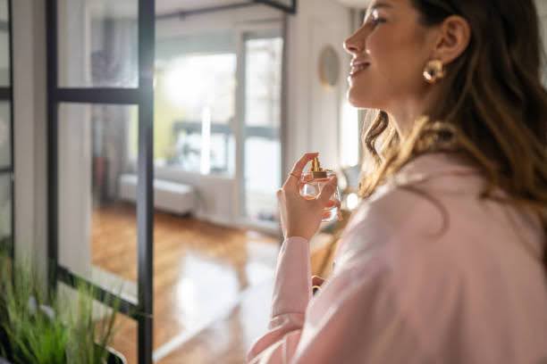 Smiling woman applying perfume in hallway while preparing to go out Smell Good All Day Long